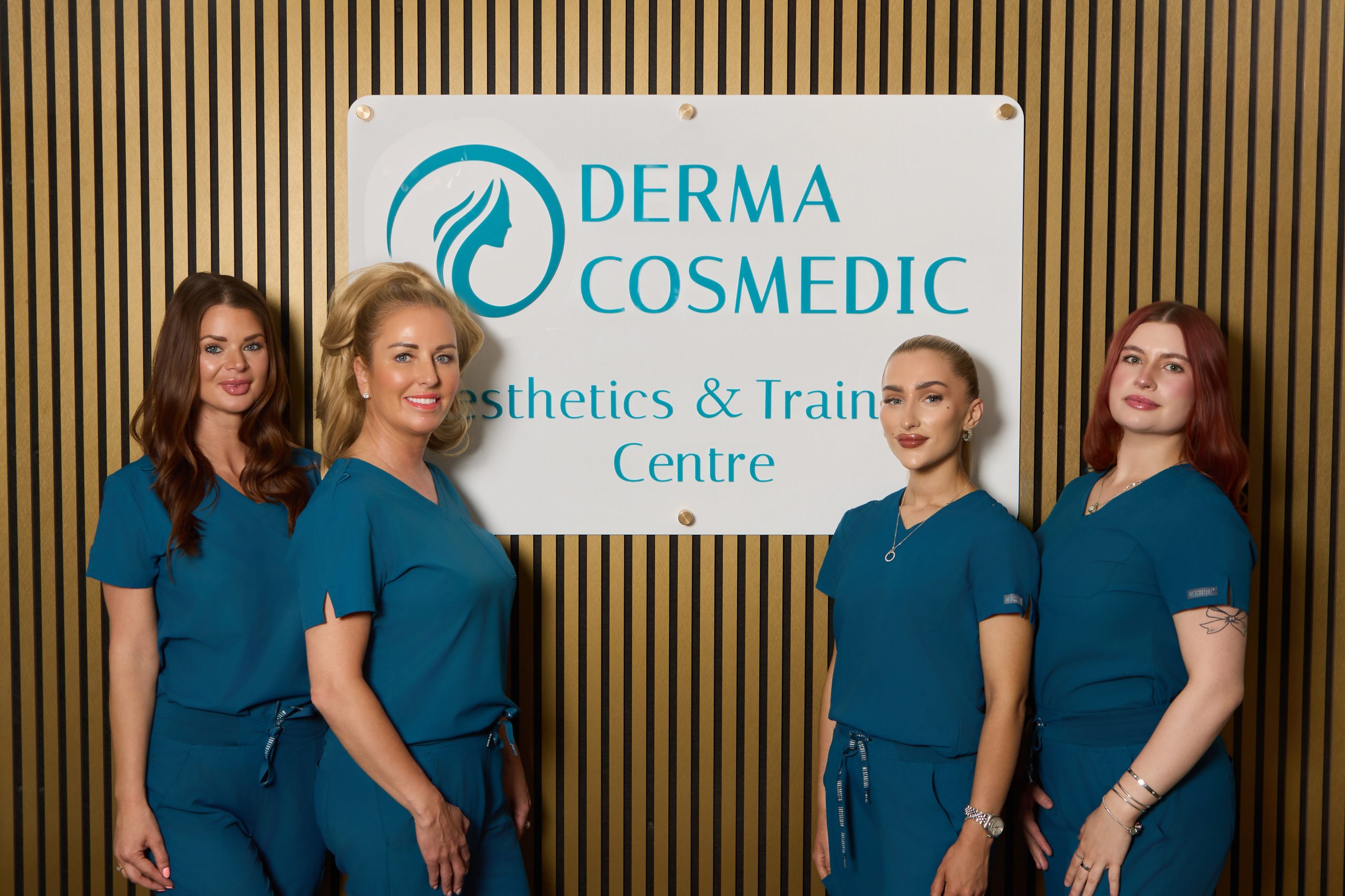 Derma Cosmedic team of four aesthetic practitioners in teal scrubs in front of the Derma Cosmedic Aesthetics & Training Centre sign at the Castle Street clinic in Liverpool