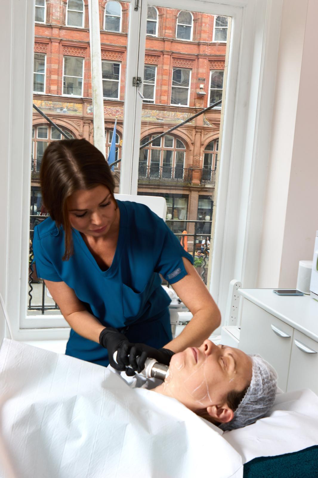 Derma Cosmedic practitioner delivering a HIFU non-surgical face lift treatment to a female client at the Castle Street Liverpool clinic, ultrasound handpiece on the mid-face with markup grid on the skin